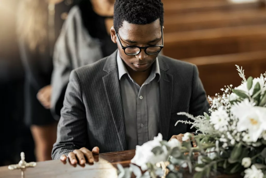 A man in a suit and glasses is at a funeral after he reported the death to social security.