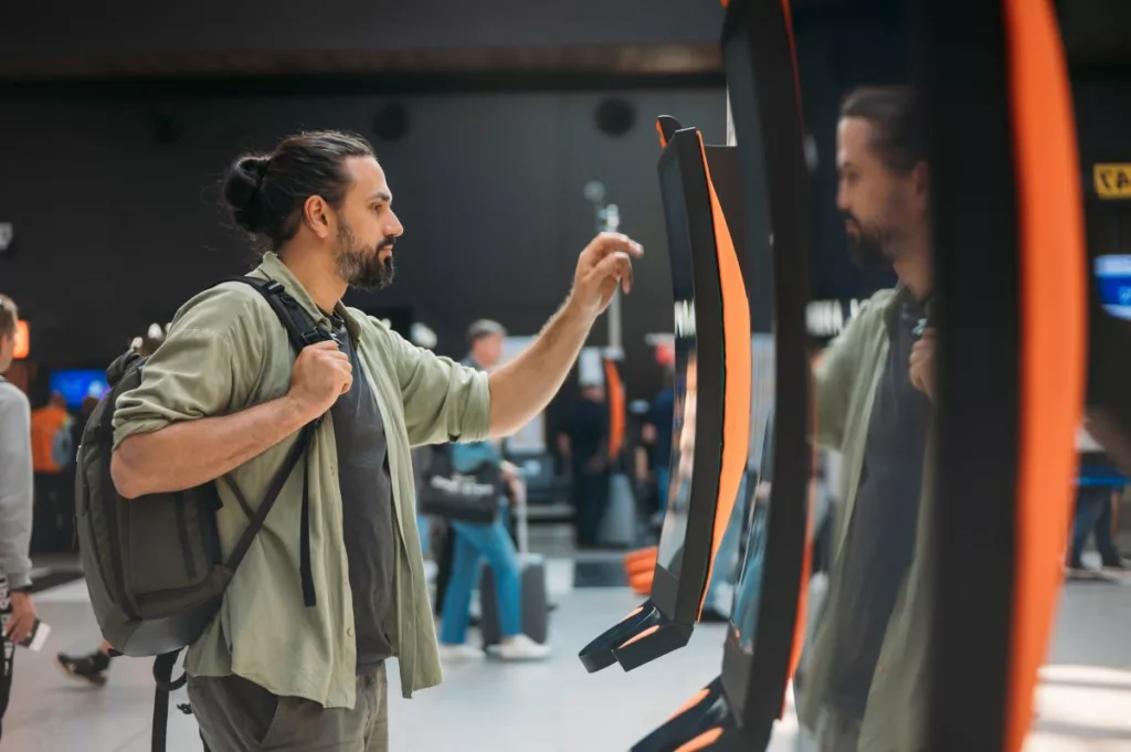 A traveler with a backpack uses an airport kiosk, representing the Repatriation Program in California, which helps residents return home during emergencies.