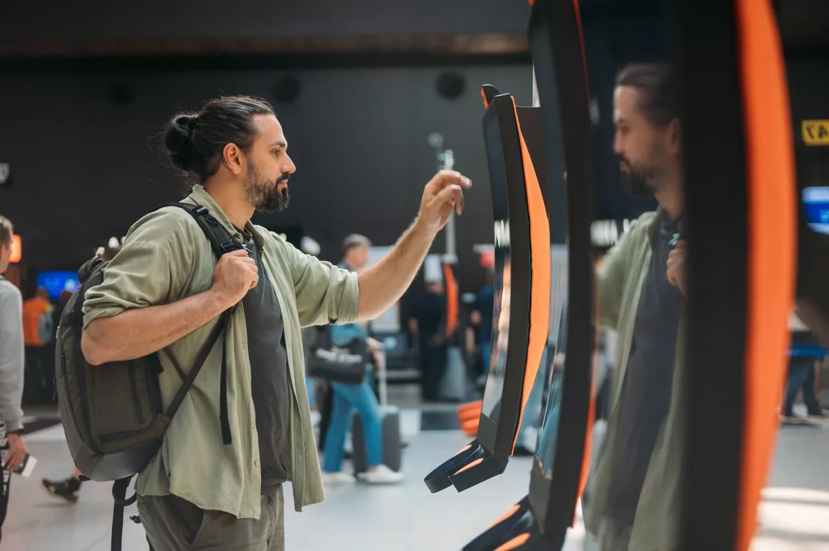 A traveler with a backpack uses an airport kiosk, representing the Repatriation Program in California, which helps residents return home during emergencies.